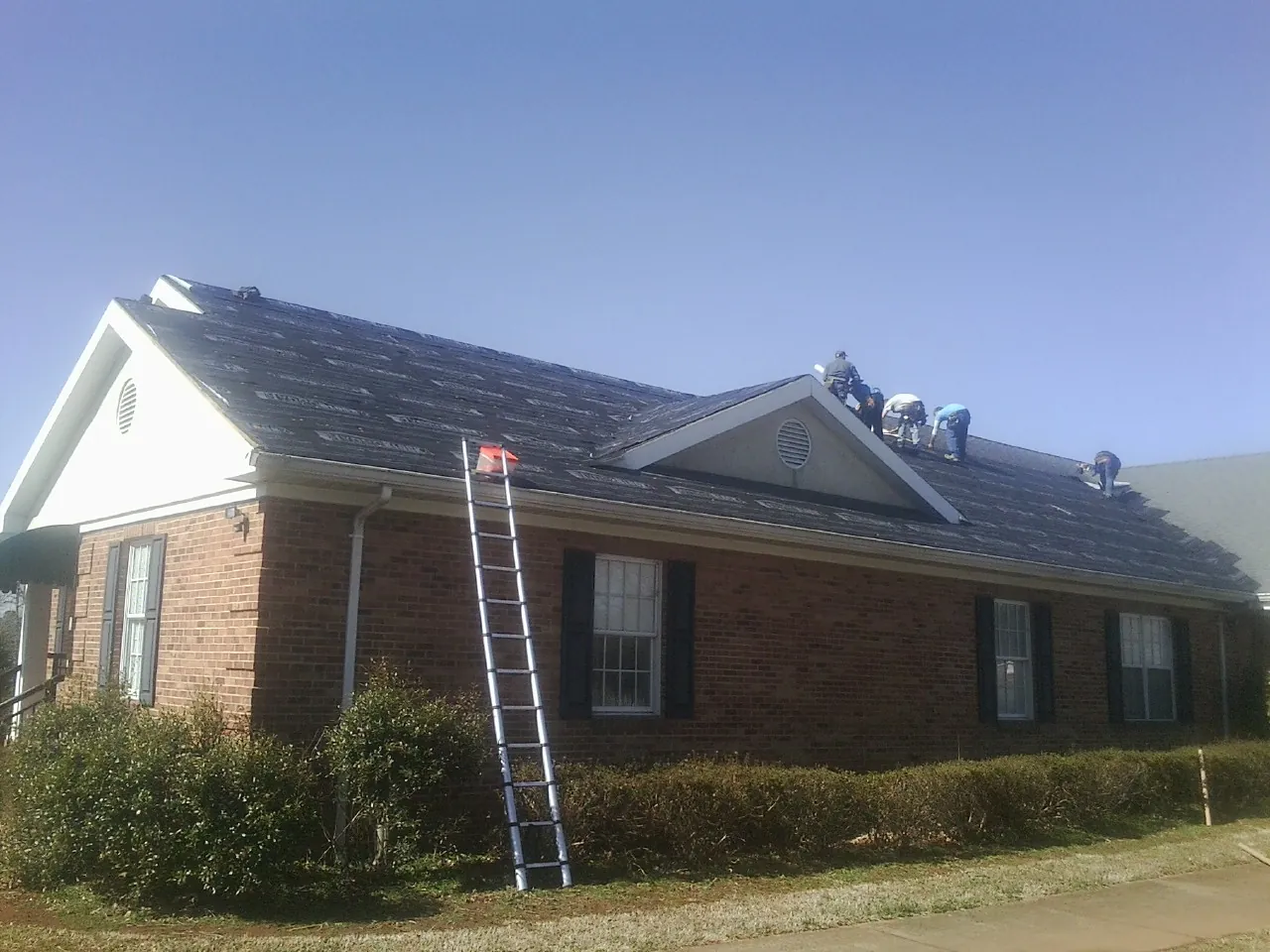 Crew tearing shingles off a brick ranch roof with a ladder set — Metal Roof Repair work by our crew in Spencertown