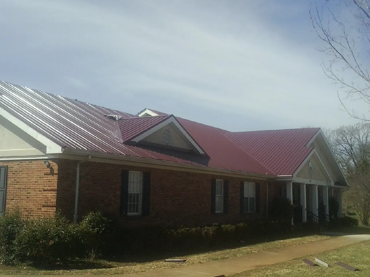 Red metal roof with gabled entries on a long brick building, from a Hail Damage Roof Repair job in Spencertown