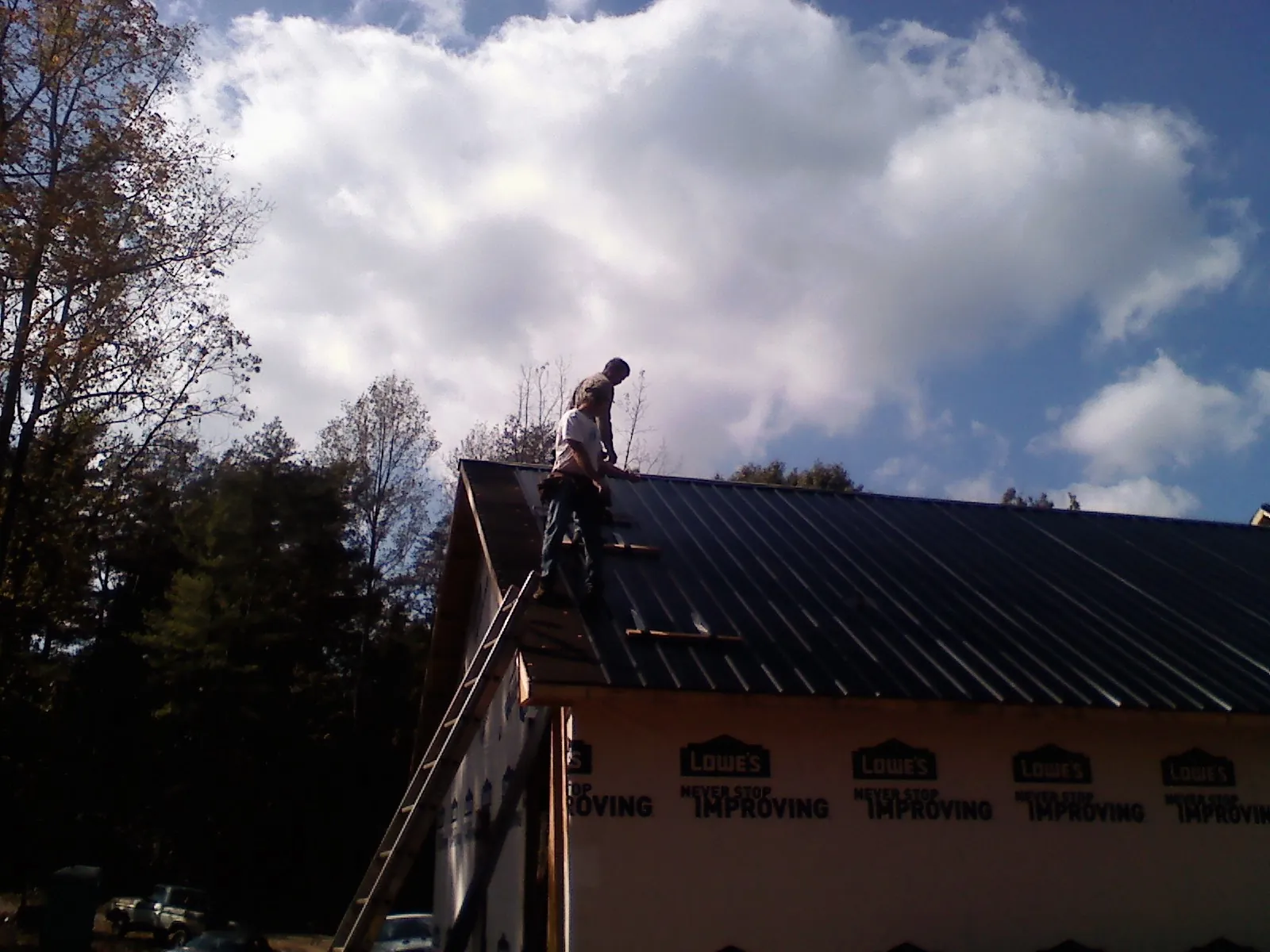 Roofer fastening dark metal panels high against a cloudy sky, from a Roof Inspection job in Spencertown