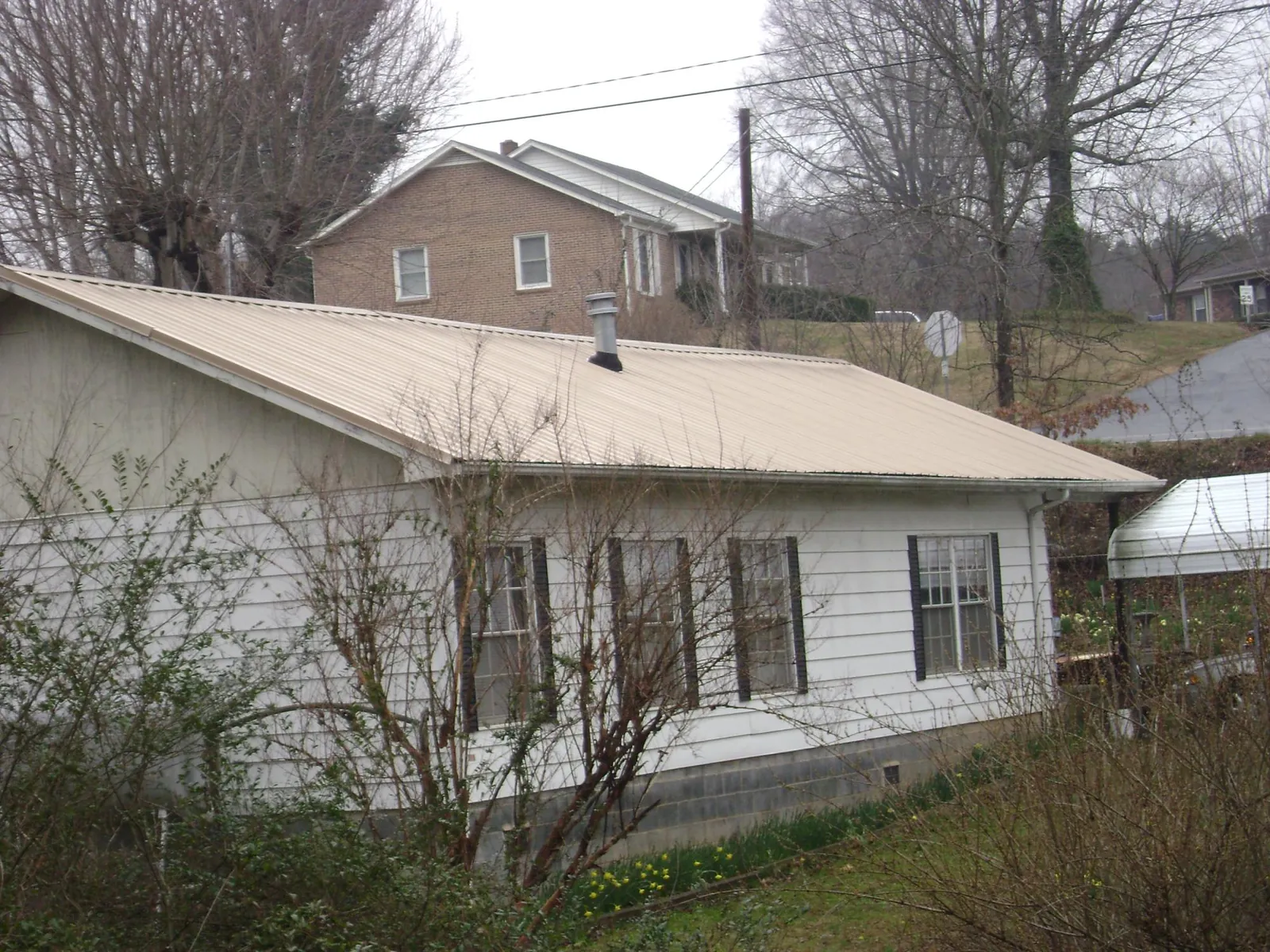 Tan metal roof on a white sided house set into a hillside — Commercial Roofing by Roofing Brothers in Spencertown